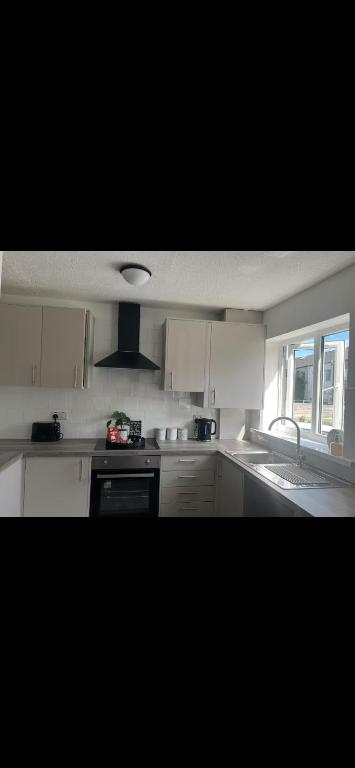 Una cocina con gabinetes blancos y un fregadero y una ventana. en Home away from home, en Bury