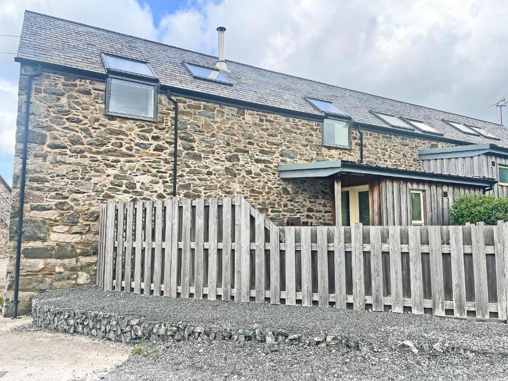 a stone house with a wooden fence in front of it at Smithy Barn - Hw7592 in Bettws-yn-Rhôs
