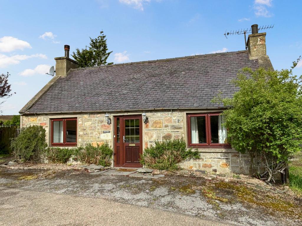 ein altes Steinhaus mit brauner Tür und Fenstern in der Unterkunft Honey Cottage in Auchnarrow