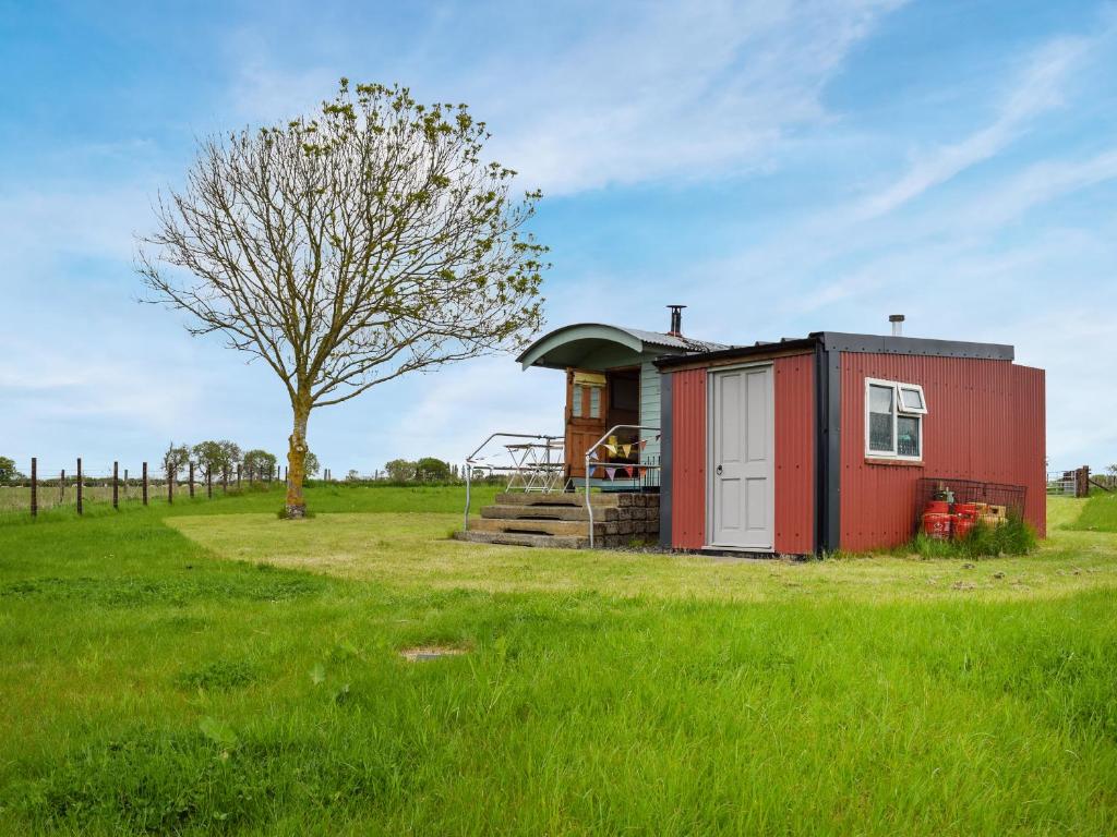 ein kleines rotes Haus auf einem Feld mit einem Baum in der Unterkunft Shepherds Cottage - Uk49766 in Northampton