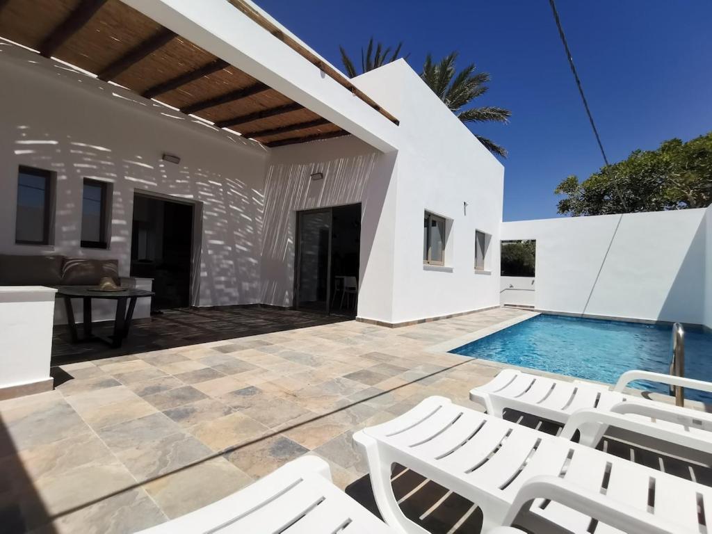 Un patio con sillas blancas y una piscina. en Au cœur de Demina, en Demina