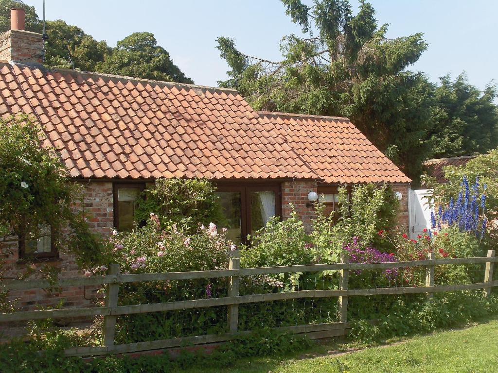 ein Backsteinhaus mit Zaun und Blumen in der Unterkunft Wisteria Cottage in Skirpenbeck