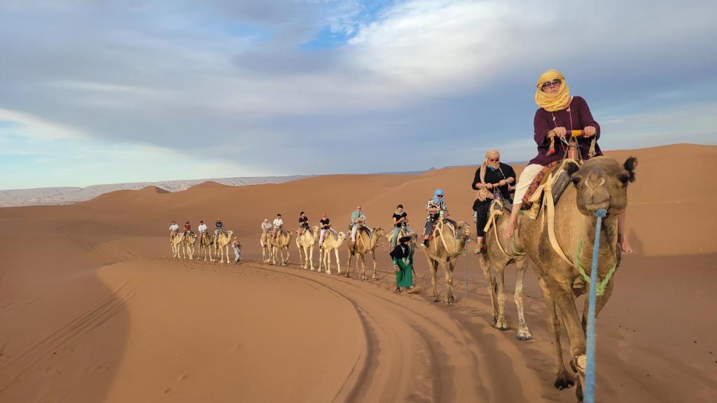 a group of people riding on camels in the desert at Mhamid camp happy night in Mhamid