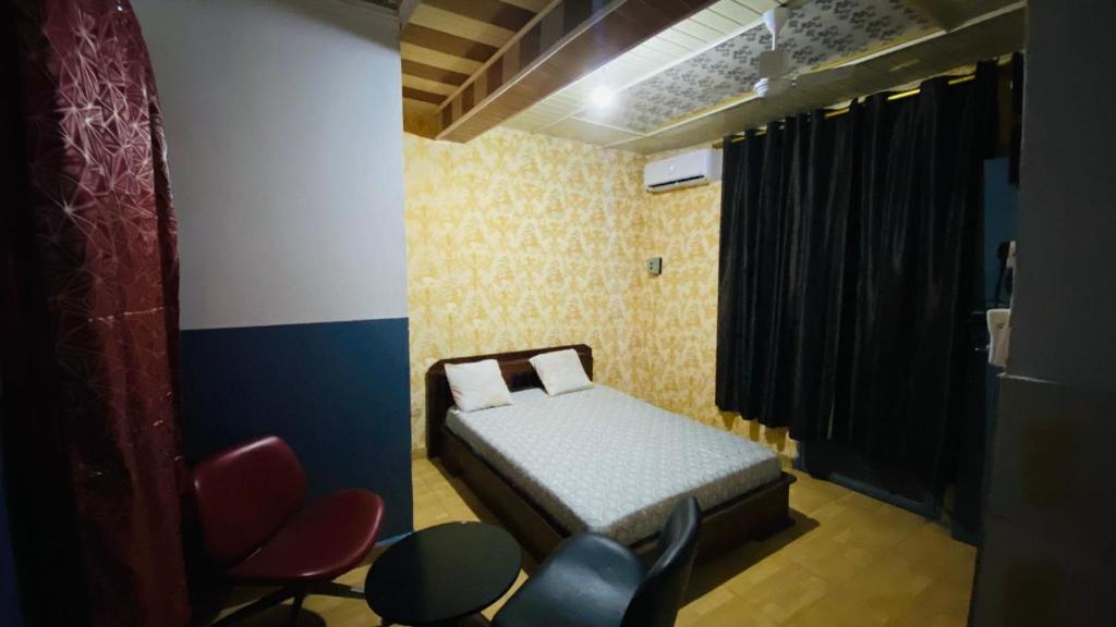 a small bedroom with a bed and some chairs at Flat Hôtel Alpha in Kinshasa