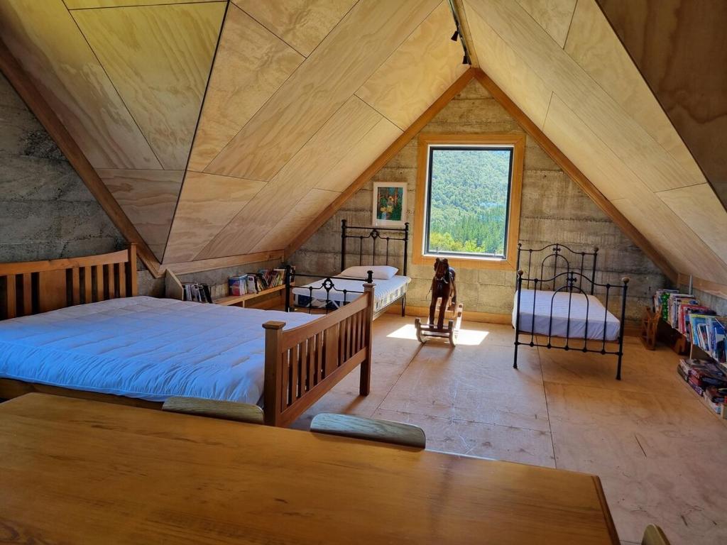 - une chambre mansardée avec 2 lits et une fenêtre dans l'établissement Pikikirunga House, Takaka Hill, à Upper Takaka