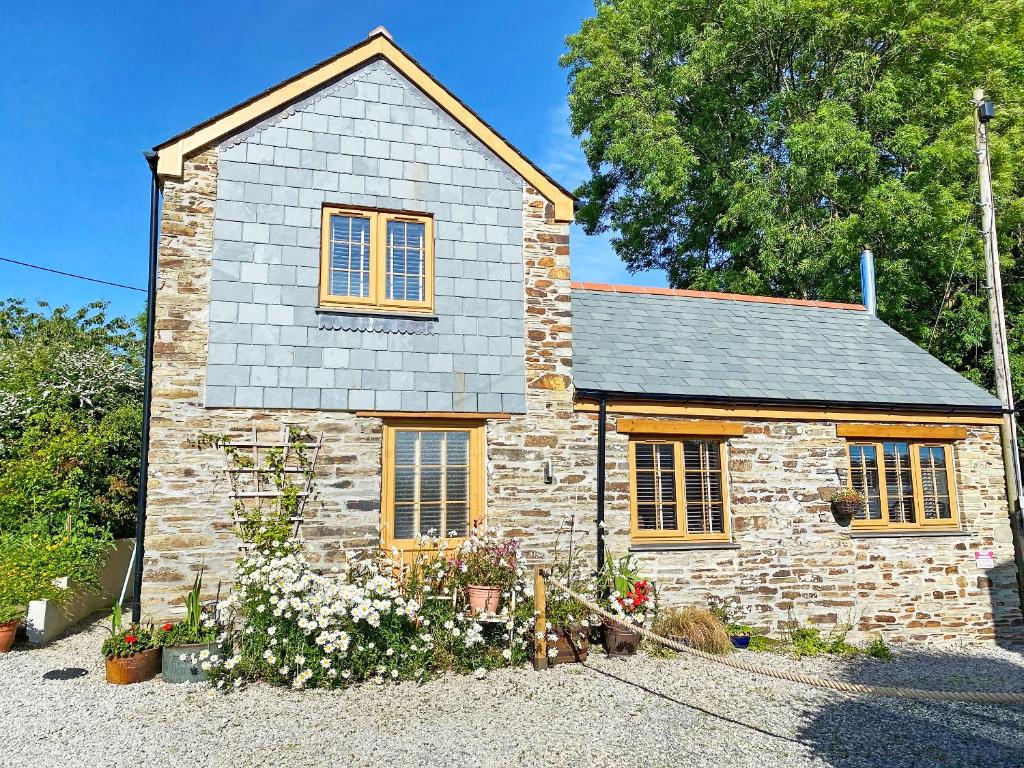 a small stone house with yellow windows and flowers at The Old Sawmill Sunnyside in Dobwalls