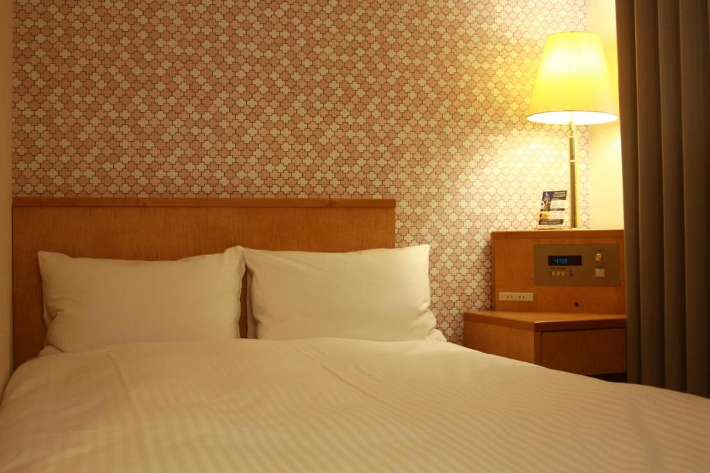 een slaapkamer met een bed en een lamp aan de muur bij Hotel Premium Green Sovereign in Sendai