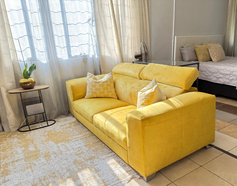 ein gelbes Sofa im Wohnzimmer mit einem Bett in der Unterkunft Cozy Garden Cottage in Johannesburg