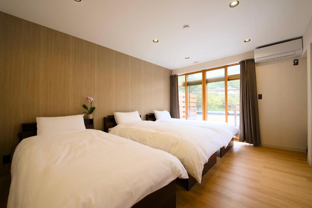 une chambre avec deux lits avec des draps blancs et une fenêtre dans l'établissement 康郷 箱根湯本, à Hakone