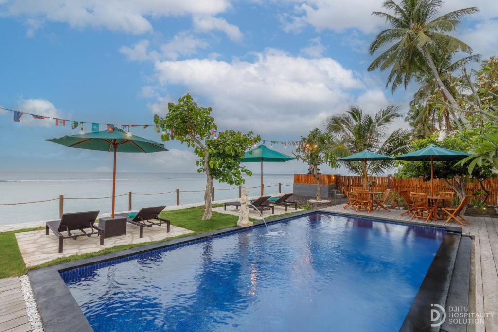 a swimming pool with chairs and umbrellas next to the ocean at La Semaya Beach Villas in Nusa Penida