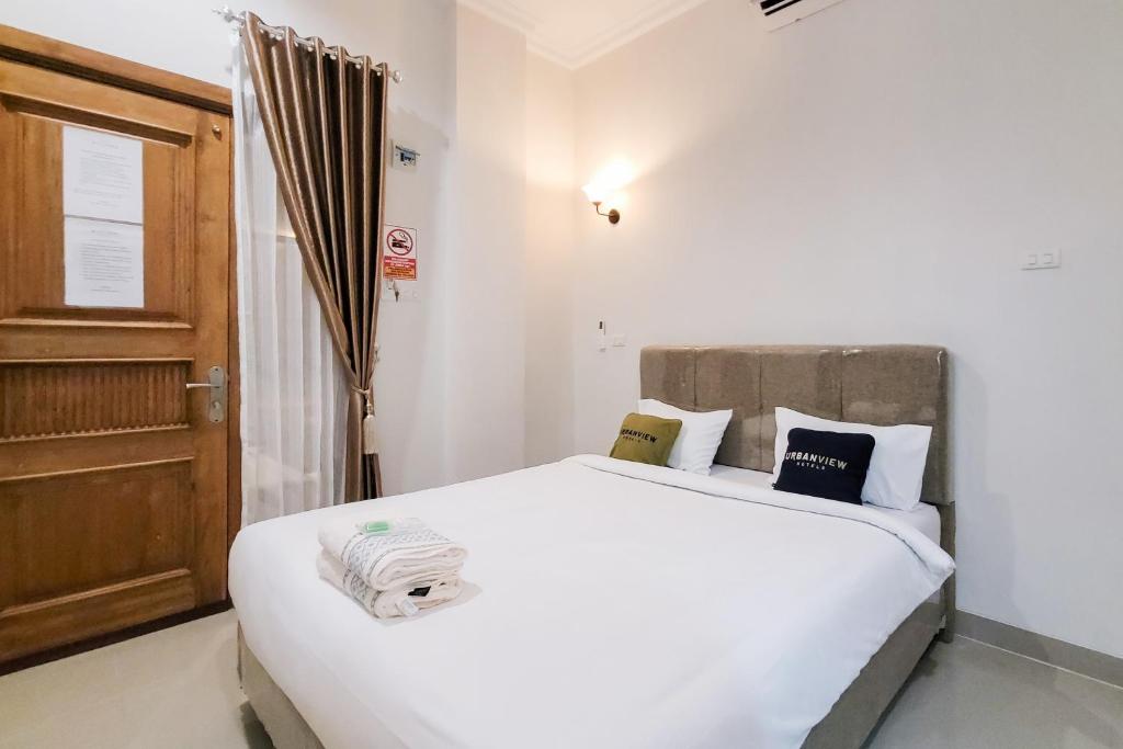 a bedroom with a white bed and a wooden door at Urbanview Hotel Bonetta Lampung by RedDoorz in Kedaton