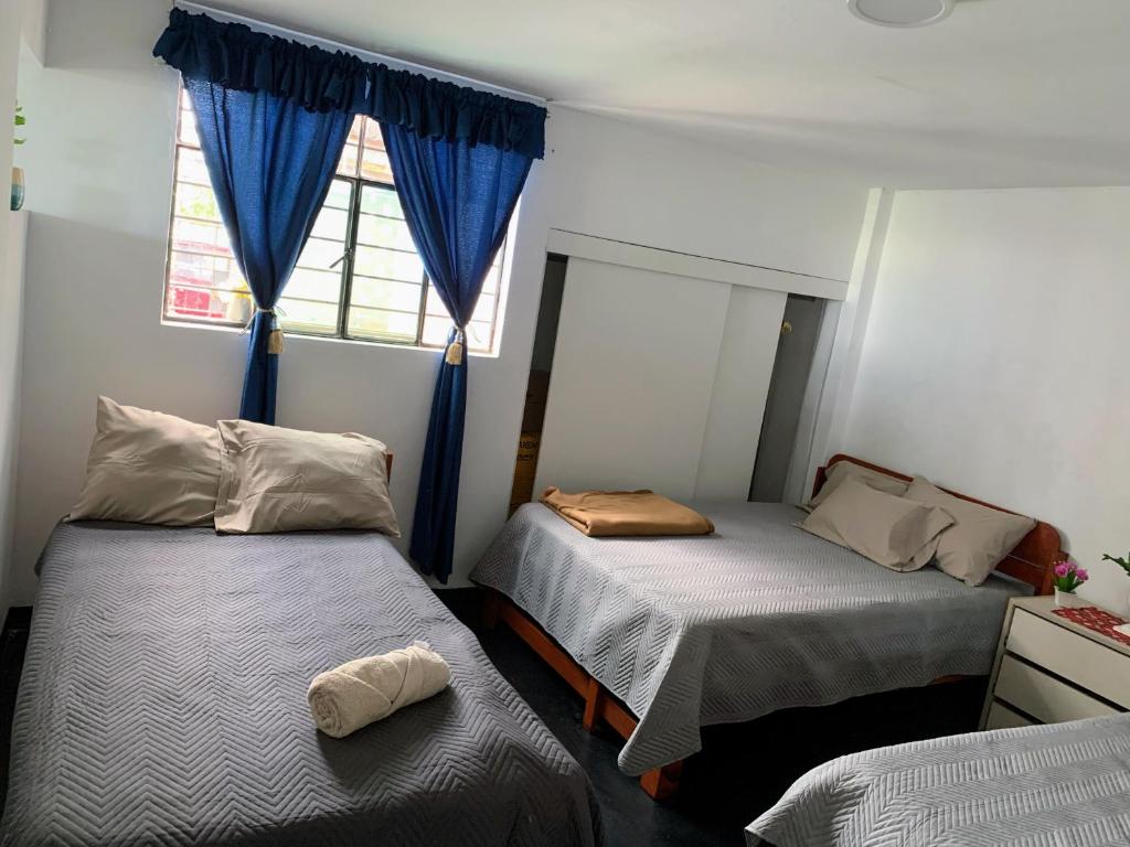 a bedroom with two beds and a window with blue curtains at HOSPEDAJE don VICTOR in Chancayllo