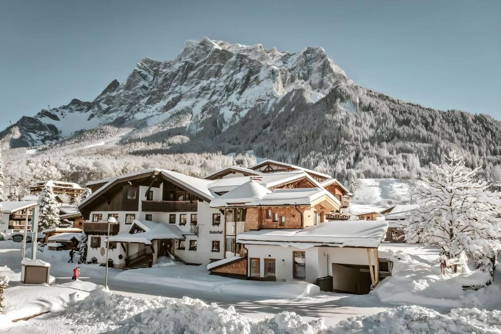 een huis bedekt met sneeuw met een berg op de achtergrond bij Hotel Tirolerhof - Familotel Zugspitze in Ehrwald