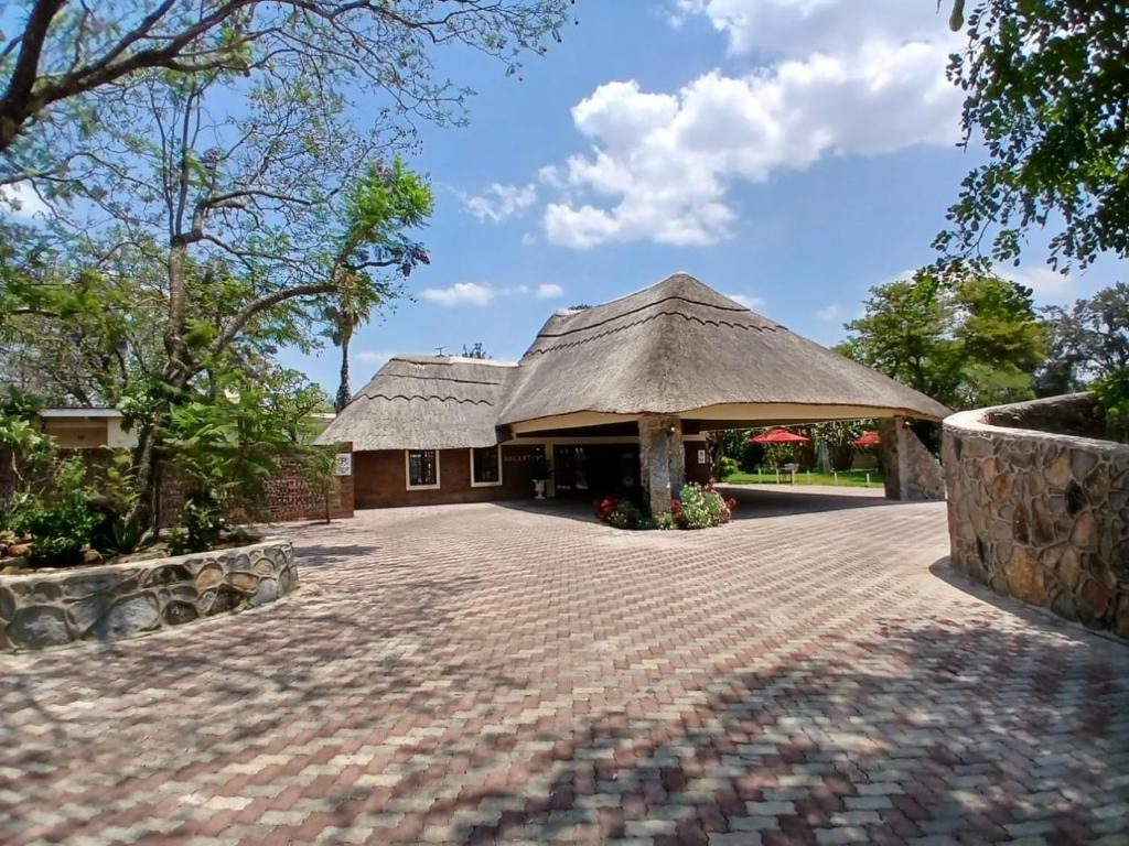 a building with a thatched roof and a brick driveway at Fortunesgate Lodge in Bulawayo
