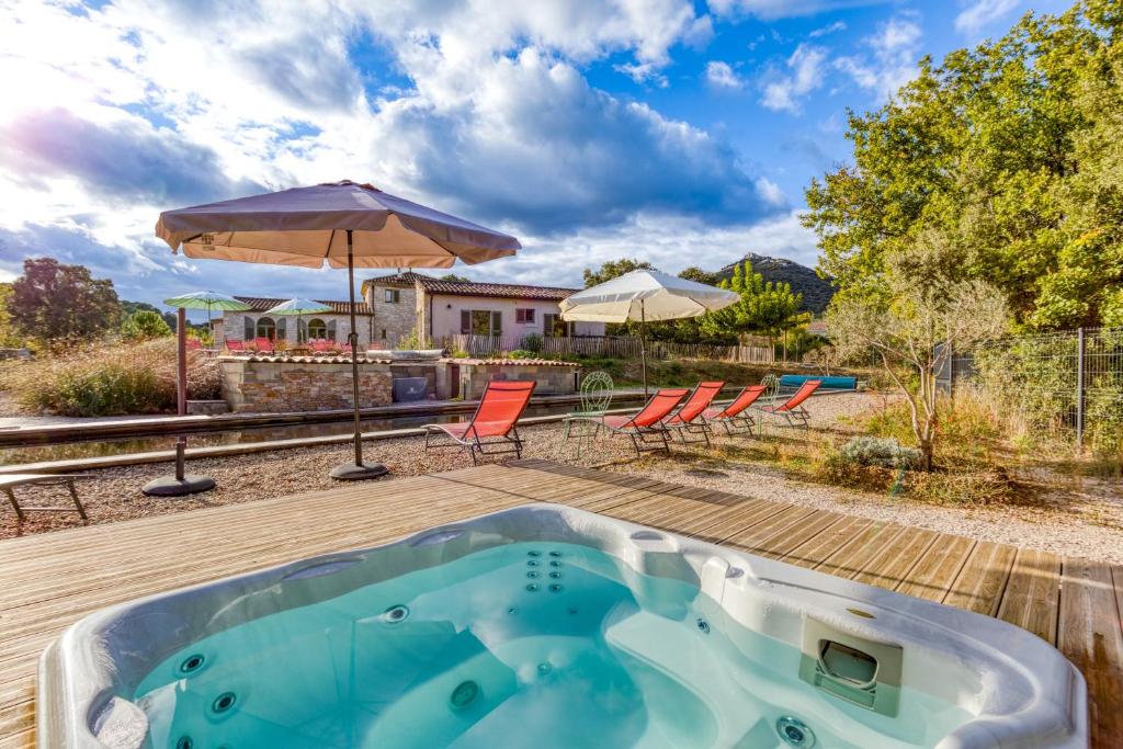 einen Whirlpool auf einer Terrasse mit Stühlen und Sonnenschirmen in der Unterkunft Gîte avec piscine de 25 m et spa in Saint-Mathieu-de-Tréviers