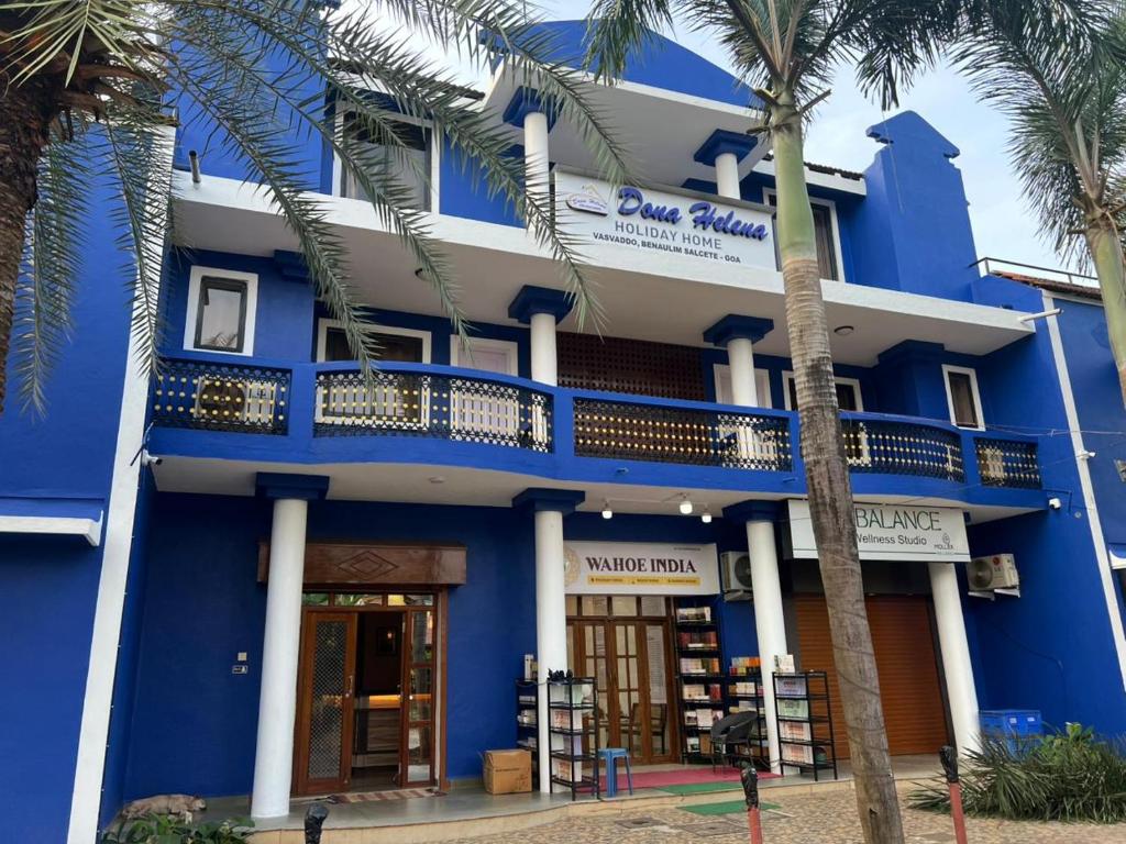 a blue building with palm trees in front of it at Dona Helena Holiday Home in Madgaon