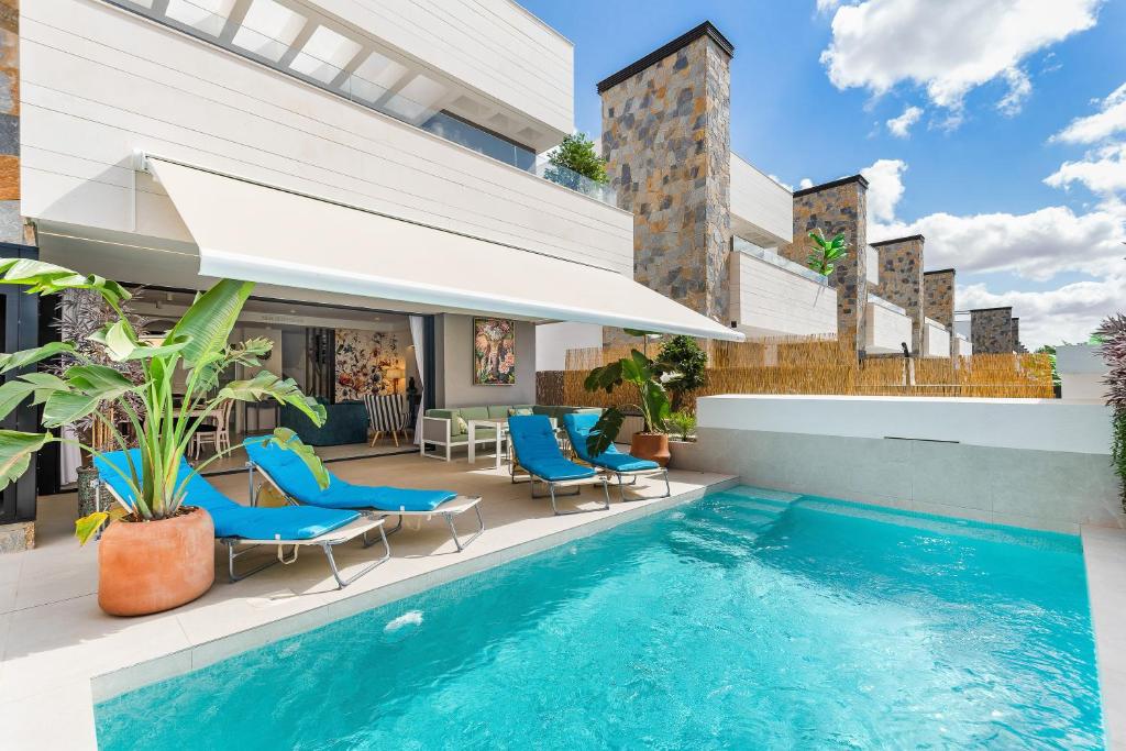 an outdoor swimming pool with blue chairs and a house at Villa de lujo con jacuzzi, cine, billar y futbolín in Las Casicas