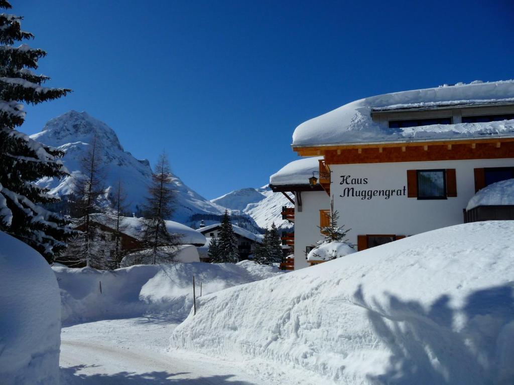 a snow covered building with a mountain in the background at Pension Muggengrat in Lech am Arlberg