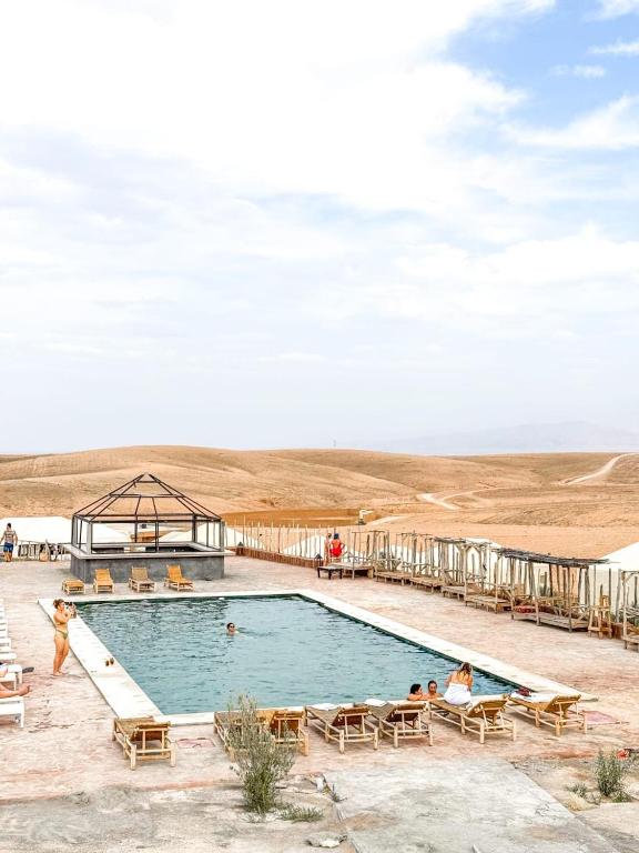 a swimming pool with chairs and people sitting around it at The Original Camp Agafay - Restaurant, Fire Show and Pool in Aït Daoud