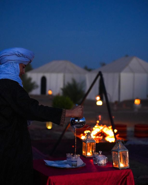 a woman pouring a glass of wine in front of a table at Merzouga Guest Camp in Merzouga
