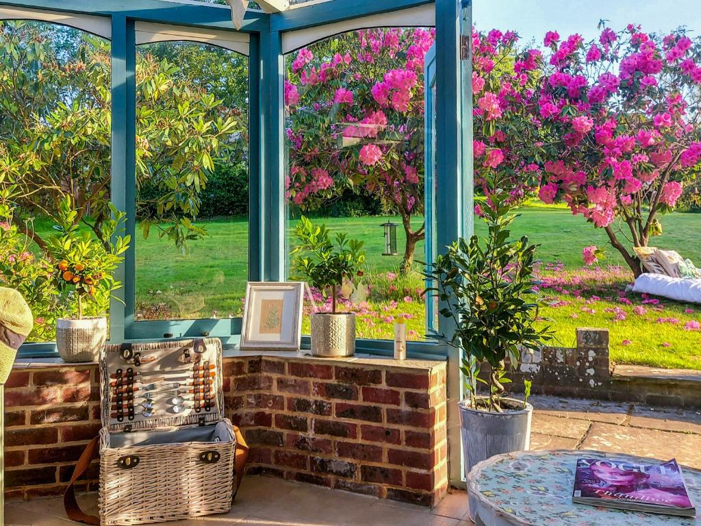 ein Wintergarten mit Blick auf einen Garten mit rosa Blumen in der Unterkunft Kipling Cottage in Burwash