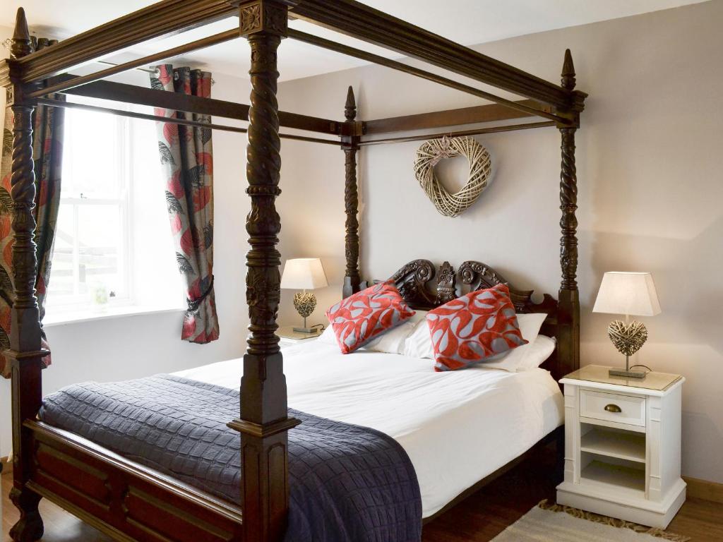 a bedroom with a four poster bed with red pillows at The Coach House in Whittingham