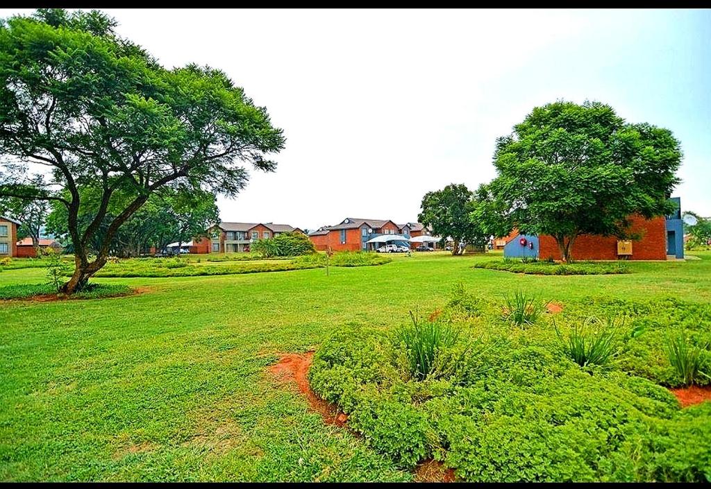 a field of green grass with a tree and houses at M Gold Apartments in Pretoria