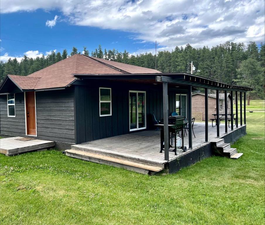 a black house with a wooden deck in the grass at Black Hills Glamping Cabin, Perfect for an Outdoor Adventure in Hill City