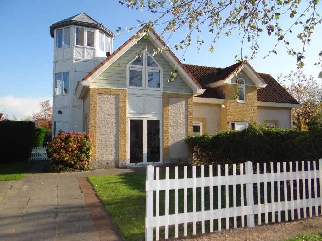 a white fence in front of a house with a clock tower at Vakantievilla Noordzee in Kamperland