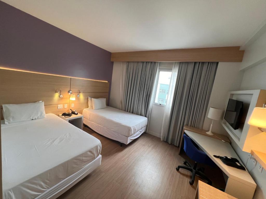 a hotel room with two beds and a desk at Flats na praia com AC, piscina, sauna e academia! in Santos