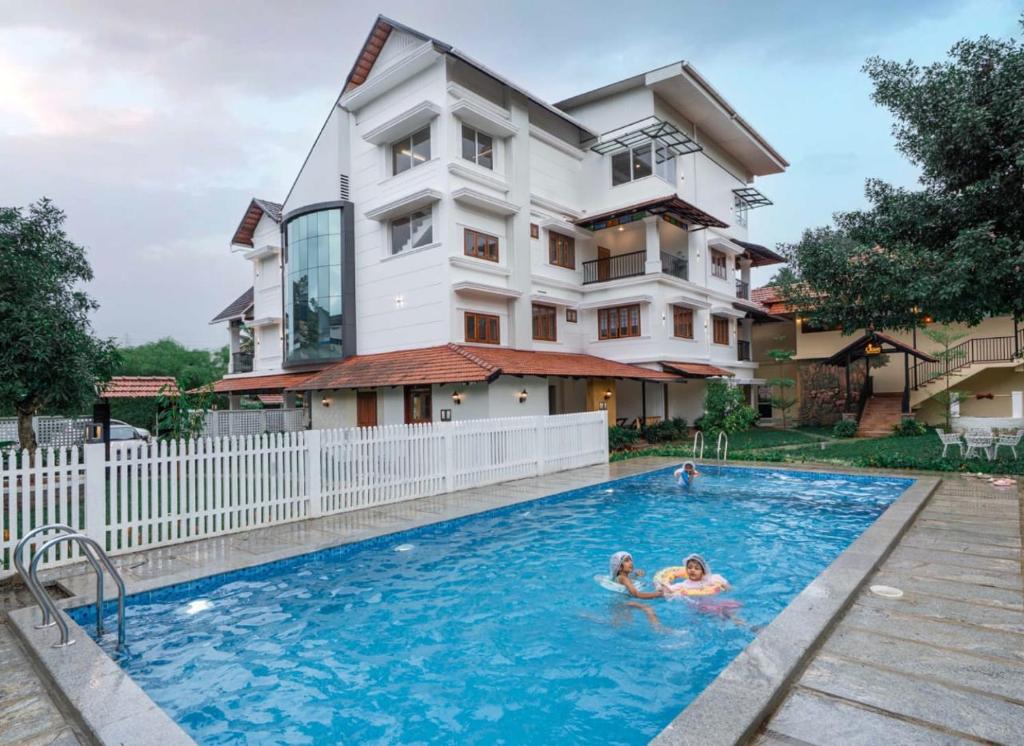 two people swimming in a swimming pool in front of a building at Citadel Boutique Hotel Thekkady in Jāmb