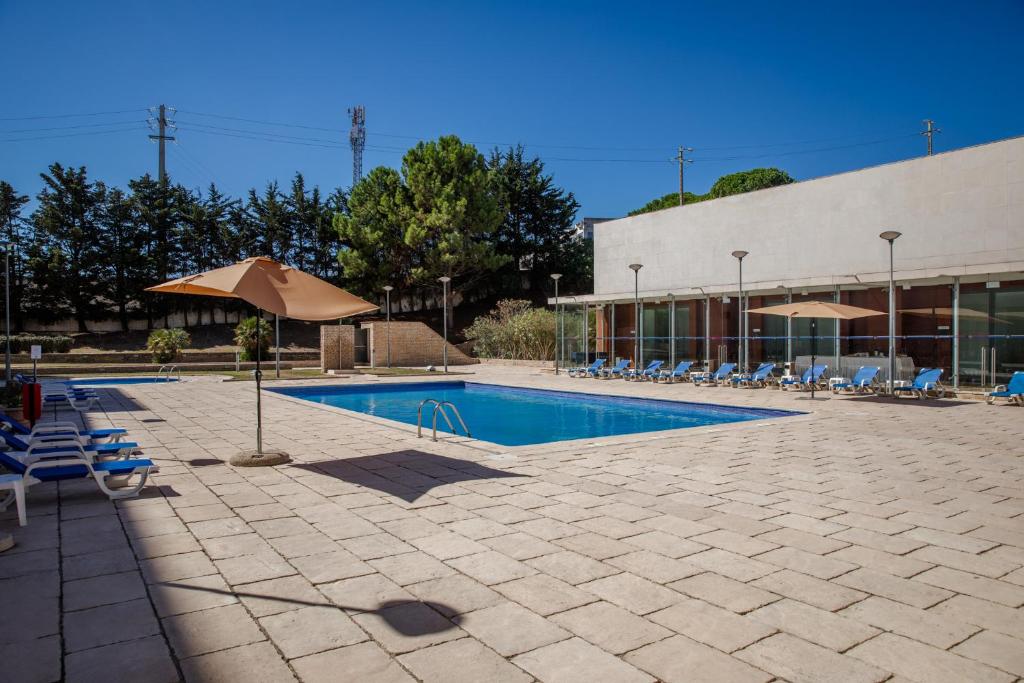 a swimming pool with chairs and an umbrella next to a building at VIP Executive Santa Iria Hotel in Santa Iria da Azóia