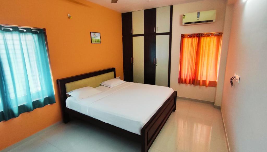 a bedroom with a white bed with orange walls and windows at RBS NEST in Tiruchchirāppalli