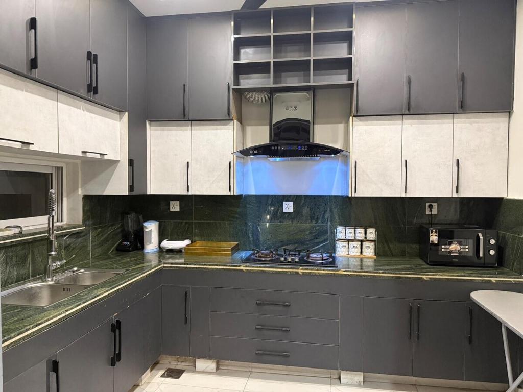 a kitchen with white cabinets and a stove top oven at Cozy 3BR Entire Home In DHA Rahbar Lahore in Lahore