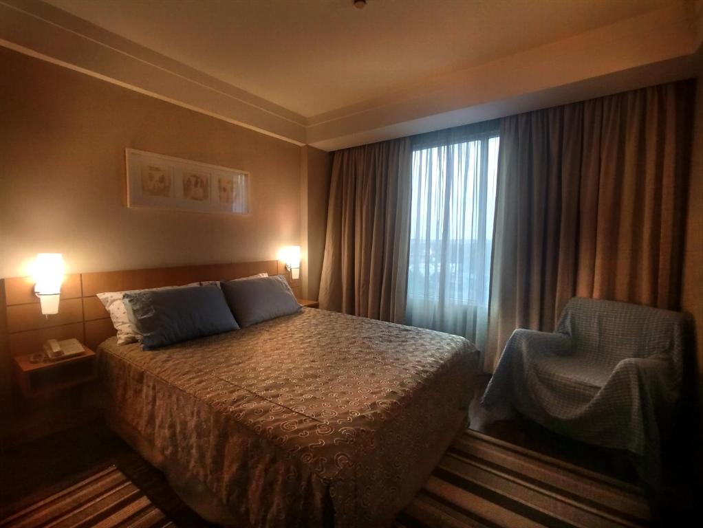 グアルーリョスにあるHotel Guarulhos Flat 902のベッドと椅子と窓のある寝室