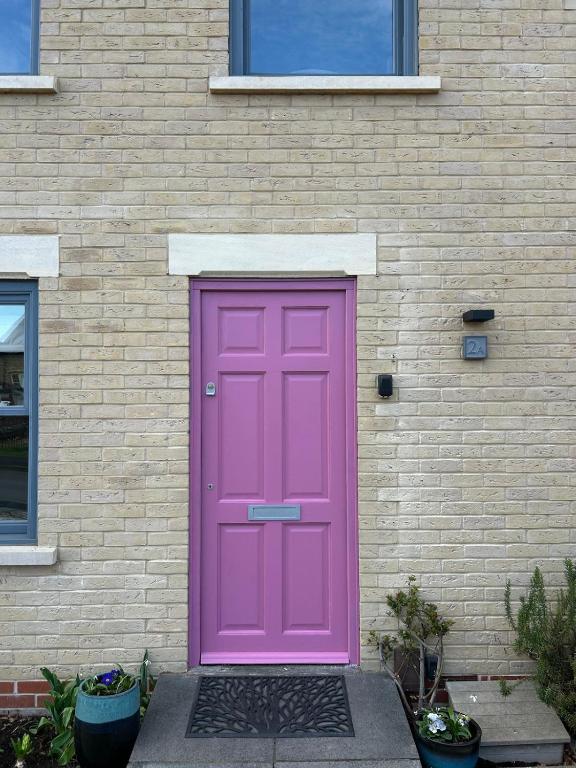 a pink door on the side of a brick building at Meadow Cottage Cambridge in Trumpington