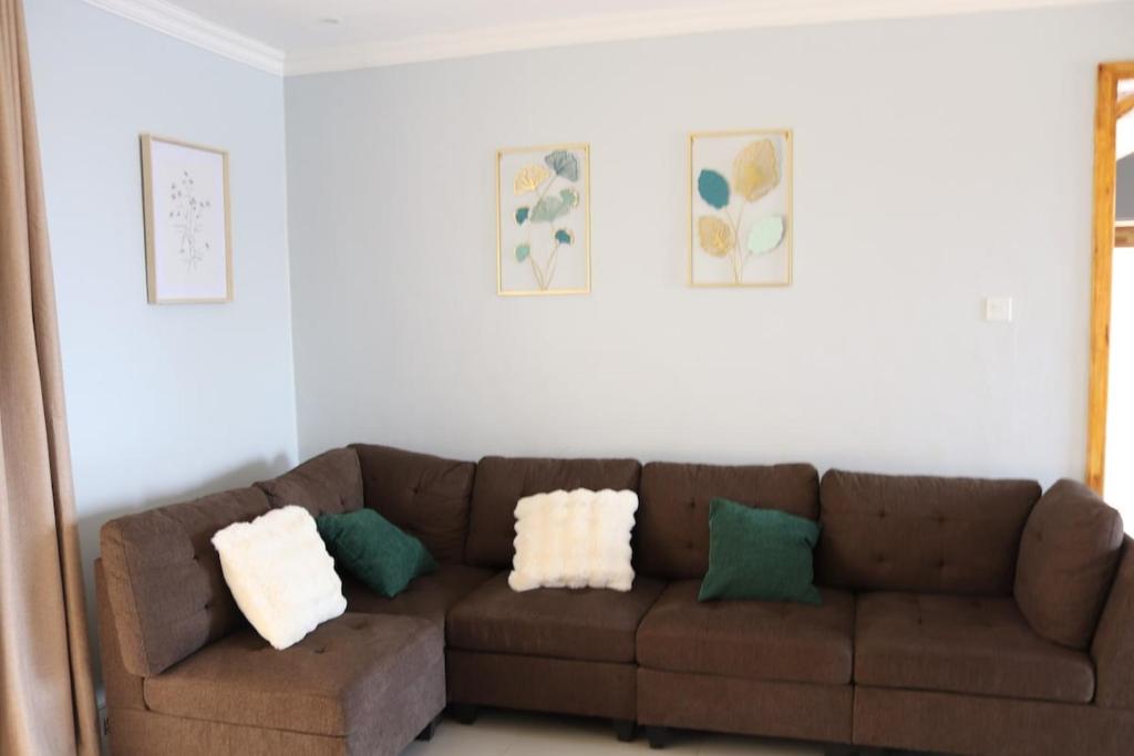 a living room with a brown couch with green and white pillows at Tical Apartments in Lilongwe