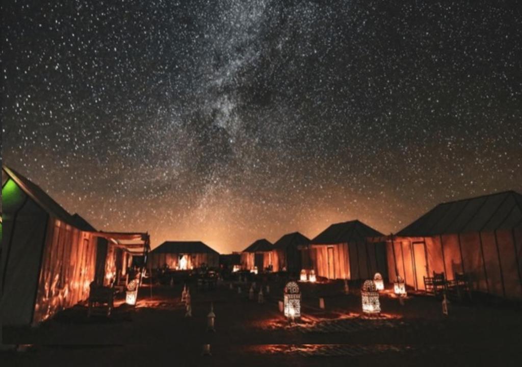 a starry night with a group of huts and the milky way at Eternal Luxury Camp in Merzouga