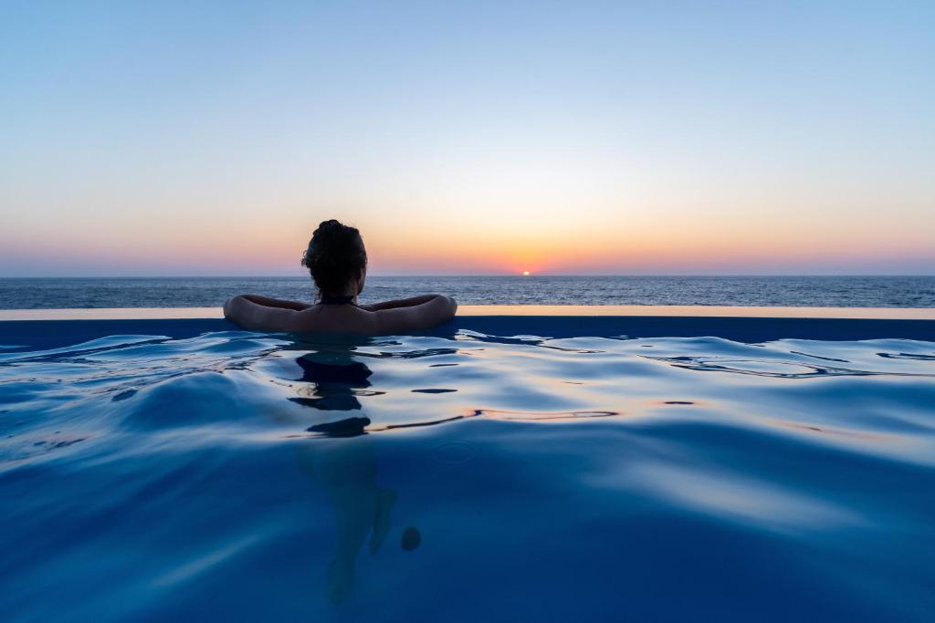 a person sitting in a infinity pool watching the sunset at Ikarian Endless Blue in Kouniádhoi