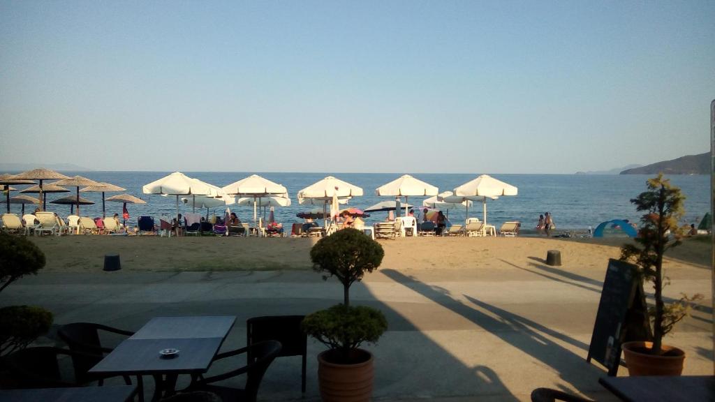 una playa con mesas y sombrillas y el océano en Bella Vista Apartments en Nea Vrasna