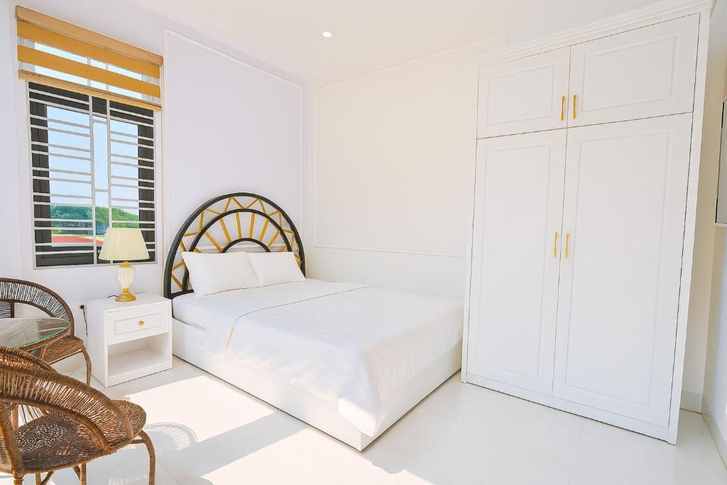 a white bedroom with a bed and a chair at King Hotel Hải Phòng in Hai Phong
