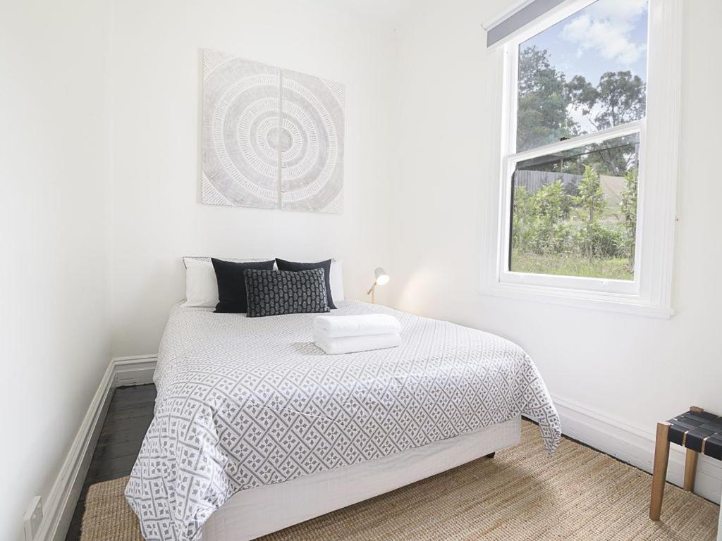 a white bedroom with a bed and a window at Healesville Gardener's Cottage in Healesville