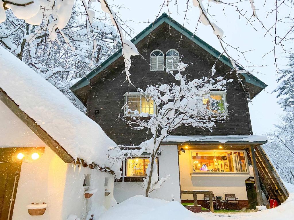 a house covered in snow with lights in the window at Pension Razteca in Hakuba