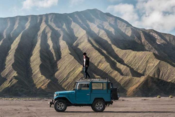 Ein Mann steht auf einem blauen Lastwagen vor einem Berg in der Unterkunft Tour Bromo in Singosari
