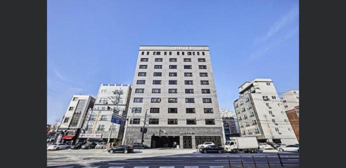 a tall white building with cars parked in a parking lot at Hoteld Benikea in Osan