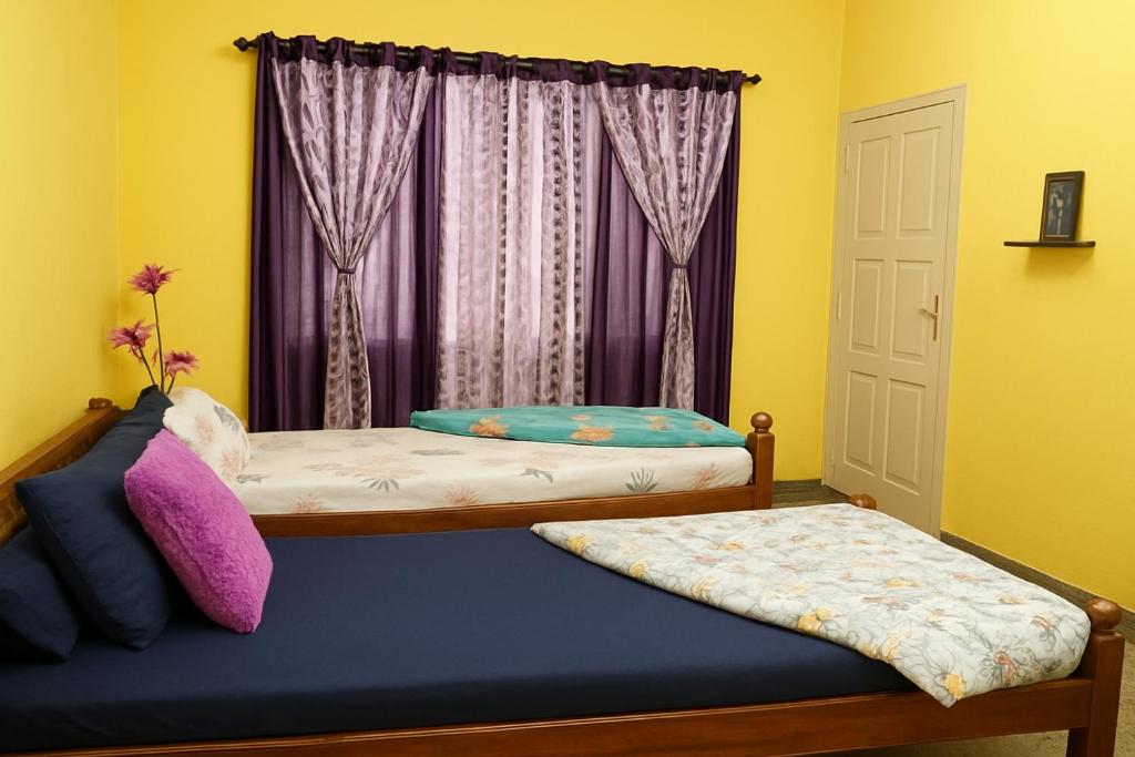 two beds in a room with yellow walls and purple curtains at Pushpa Nilaya in Madikeri