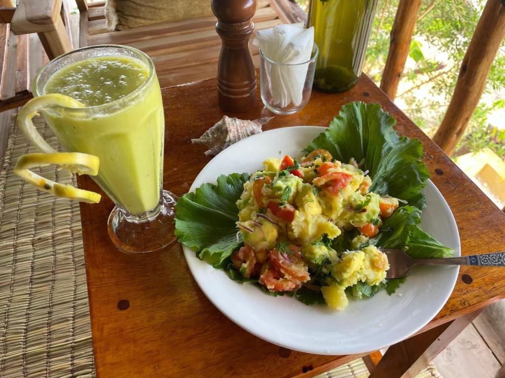 Un plato de comida con ensalada y un vaso de jugo en Serenity stay Kizimkazi, en Kizimkazi