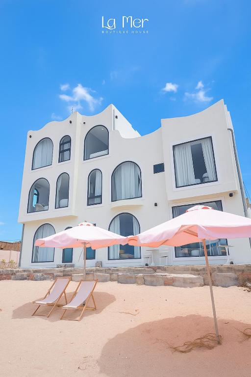 two umbrellas on the beach in front of a building at La Mer Boutique House in Cù Lao Thu