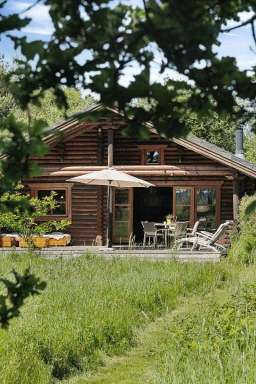 a log cabin with an umbrella and a table and chairs at Nordic Log Cabin With Views Over The Fields in Hals