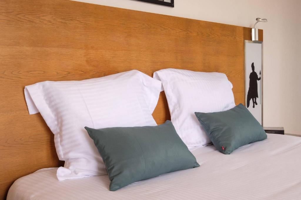 a bed with white pillows and a wooden headboard at Comfort Aparthotel Antibes Le Maestria in Antibes